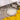 A styled tabletop setting featuring a hammered silver dinner plate with a cream center, accompanied by matching silver cutlery, small metal bowls, a metal cup, and a bright yellow fabric napkin on a textured gray surface.